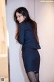 A woman in a business suit leaning against a wall.