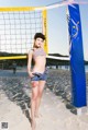 A woman standing next to a volleyball net on a beach.