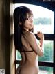 A naked asian woman leaning against a window.