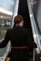 A woman in a black suit is walking down an escalator.