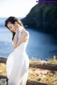 A woman in a white dress leaning against a wooden fence.