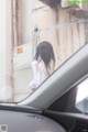 A woman standing in front of a car looking out the window.