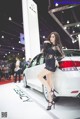 A woman in a black dress standing next to a white car.