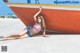 A woman in a bikini laying on the beach next to a boat.