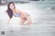 A woman in a blue and white bikini standing in the ocean.