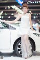 A woman in a white dress standing next to a white car.