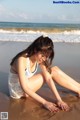 A woman sitting on the beach in a white dress.