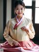 A woman in a pink and gold hanbok poses for a picture.