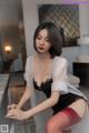 A woman in a black lingerie and red stockings sitting on a counter.