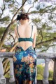 A woman in a green bra top and floral skirt standing on a balcony.