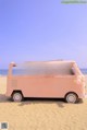 A woman sitting in the back of a pink van on the beach.