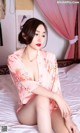 A woman in a pink kimono sitting on a bed.