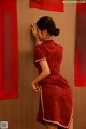 A woman in a red dress leaning against a wall.