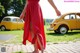 A woman in a red dress standing in front of a yellow car.