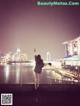 A woman standing on a bridge looking at the city at night.