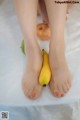 A woman's feet with a banana and an apple on a bed.