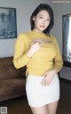 A woman in a yellow sweater and white skirt posing for a picture.