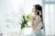 A woman in a white dress holding a bunch of white flowers.