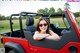 A woman sitting in the driver's seat of a red jeep.