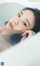 A woman laying in a bathtub with her hand on her chin.